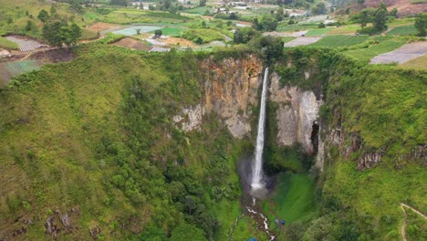 Aerial-view-of-Sipiso-Piso-Waterfall-and-colourful-fields-in-North-Sumatra,-Indonesia