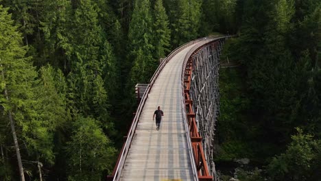 Aerial-Drone-Chase-of-Man-Running-Across-Large-Bridge-in-Forest---Kinsol-Trestle,-Vancouver-Island
