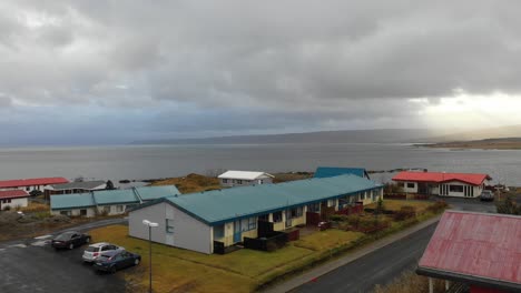 Drone-Volando-Sobre-Casas-Costeras-Multicolores-Sobre-El-Océano-Revelando-Una-Impresionante-Puesta-De-Sol-Sobre-Las-Montañas,-Reykjavík-Islandia