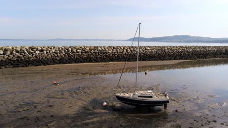 Aerial-view-boats-in-shimmering-low-tide-sunny-warm-Rhos-on-Sea-seaside-sand-beach-marina-low-dolly-right