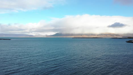 Fliegen-Vor-Der-Küste-Von-Reykjavik-In-Richtung-Wolkenbedeckter-Berge,-Bevor-Sie-Abbiegen,-Um-Die-Stadt-Zu-Enthüllen,-Drohnenantenne