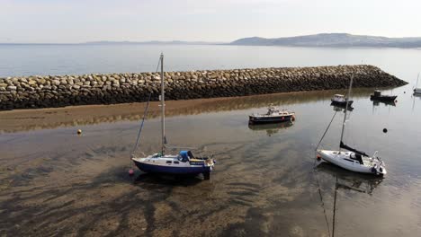 Aerial-view-boats-in-shimmering-low-tide-sunny-warm-Rhos-on-Sea-seaside-sand-beach-marina-rising-tilt-down