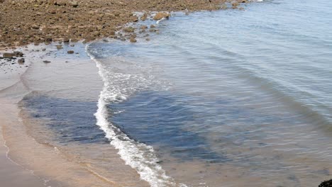 Sunny-clear-tide-waves-splash-against-pebble-coastline-shore-edge