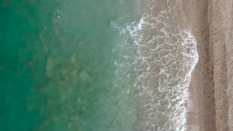 Turquoise-sea-waving-and-foaming-on-sandy-beach,-top-down-view-of-water-texture