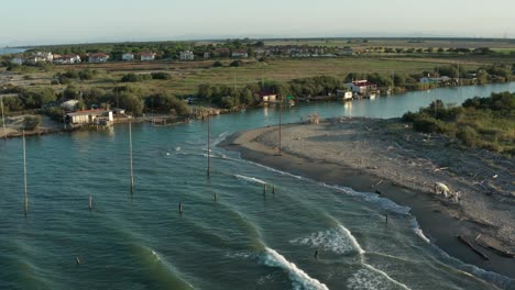 Aerial-shot-of-the-valleys-near-Ravenna-where-the-river-flows-into-the-sea-with-the-typical-fishermen's-huts-at-sunset