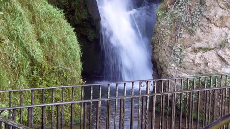 Scenic-splashing-waterfall-and-metal-guard-railing-between-idyllic-rock-formation