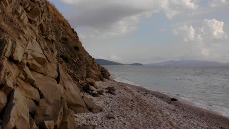 Rocky-slope-of-hills-and-pebbles-beach-washed-by-sea-on-a-cloudy-day-in-Mediterranean-scenery