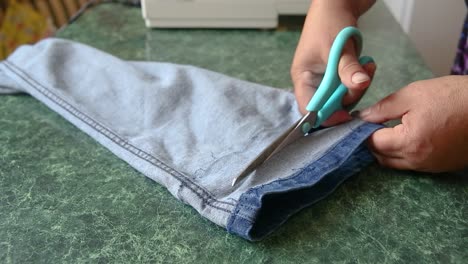 Hands-of-female-tailor-cut-jeans-leg-shorter-with-scissors,-sewing-skills