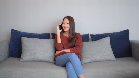 Attractive-young-woman-talking-on-a-mobile-phone-while-sitting-on-a-couch-in-her-living-room