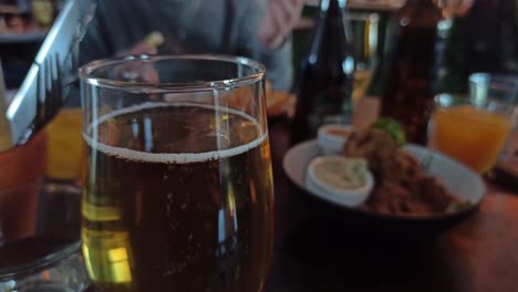 A-close-up-shot-of-a-glass-of-cider-while-people-grab-food-from-plates-in-the-background