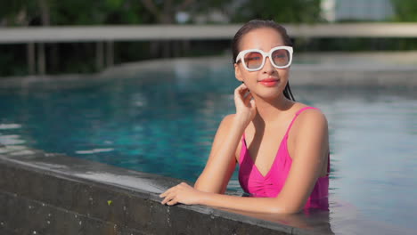 A-healthy-young-woman-in-a-pink-one-piece-swimsuit,-lounges-along-the-edge-of-an-infinity-pool