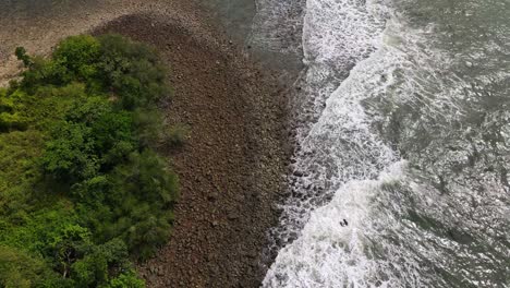 Top-view-aerial-above-island-pebble-shoreline-tide-current-surging-along-the-coastline