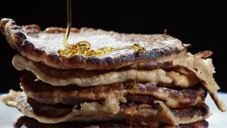 Close-up-of-syrup-being-poured-onto-stack-of-pancakes-with-icing-sugar