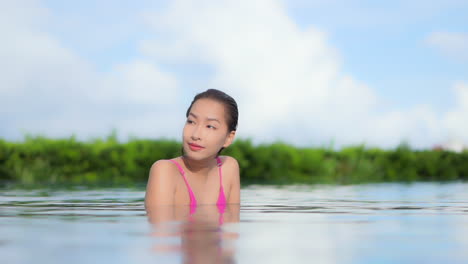 Während-Sie-Das-Wasser-In-Einem-Von-Tropischem-Grün-Umgebenen-Resort-Pool-Genießt,-Richtet-Sie-Ihre-Augen-Auf-Die-Kamera-Und-Lächelt