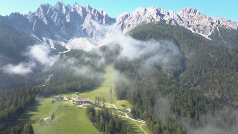 Aerial-of-a-Ski-Slope-during-Summer,-high-mountain-peaks-with-cloud-mist,-Innichen-South-Tirol