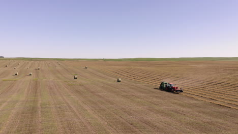 Farm-Machinery-Baling-Hay-At-The-Field-In-Saskatchewan,-Canada-After-Harvest-Season---panning-drone-shot