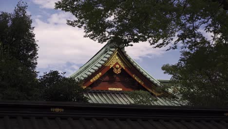 Beautiful-Japanese-red-and-gold-temple-against-blue-cloudy-sky-silhouetted-between-trees---locked-off-shot