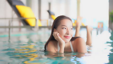 Sexy-Asiatische-Frau,-Die-In-Der-Flachen-Seite-Auf-Schwimmbad-Liegt,-Nahaufnahme-Auf-Lächelndem-Gesicht,-Thailand-Resort-Spa,-Zeitlupe