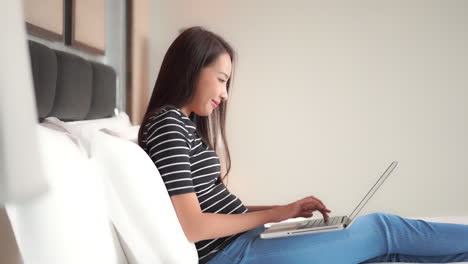 Asiatische-Frau,-Die-Im-Bett-Sitzt-Und-Auf-Laptop-computer-Tippt