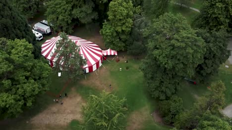 People-Walking-In-The-Park-Around-The-Circus-Tent-Surrounded-by-The-lush-Green-Trees-In-Summer
