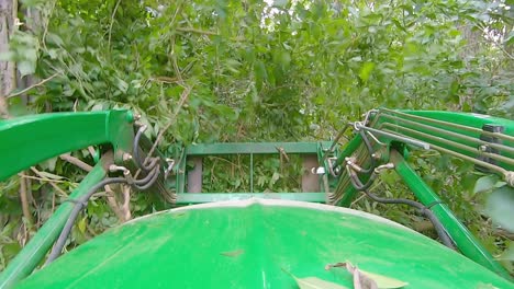 POV-of-equipment-operator-using-a-loader-with-forks-to-move-debris-and-brush-in-a-yard-surrounded-by-the-woods