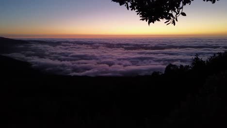 Ein-Zeitraffer-Des-Sonnenaufgangs-über-Den-Wolken-Von-Einem-Berg-Unter-Einem-Baum