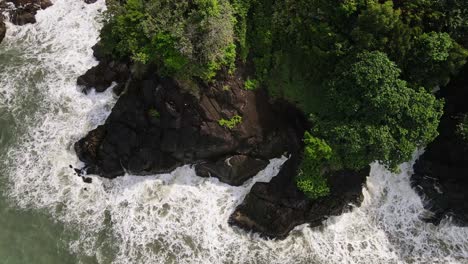 Birdseye-aerial-view-above-splashing-coastal-tide-and-dense-treetop-green-canopy-moving-inland-Thailand