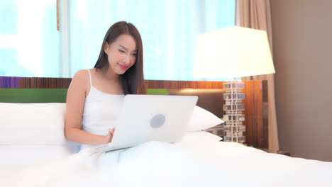Young-woman-celebrates-good-news-while-using-laptop-computer-sitting-in-bed