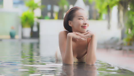 A-narrow-depth-of-field-a-lovely-young-woman-lies-on-her-stomach-on-the-shallow-edge-of-a-resort-infinity-pool-looking-off-to-her-left