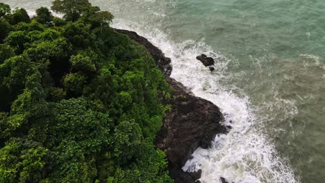 Top-view-Thailand-islands-treetop-canopy-coastline-tide-splashing-rocky-landscape-aerial-view