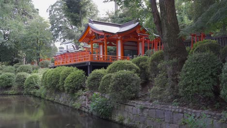 Beautiful-red-Shrine-house-at-Nezu-Shrine-in-Tokyo-next-to-pond---locked-off-view