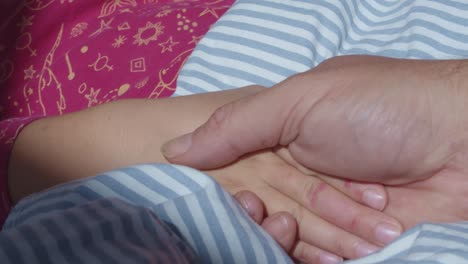 Close-up-of-father-holding-hands-with-daughter-at-bedtime-saying-goodnight-and-letting-go