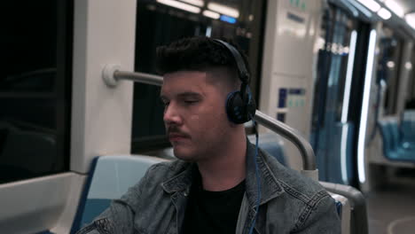 Young-Guy-Sitting-Inside-A-Moving-Train-While-Listening-Music-By-Headphones-At-The-Underground-Metro-In-Montreal,-Quebec,-Canada