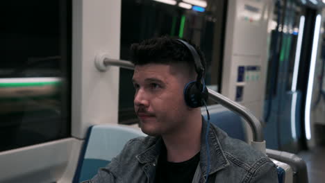 Young-Man-Sitting-Inside-A-Moving-Train-Listening-Music-By-Headphones-While-Travelling-At-The-Underground-Metro-In-Montreal,-Quebec,-Canada