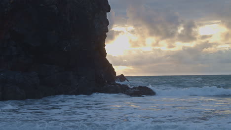Waves-crash-on-cliffs-silhouetted-by-blazing-sun-through-clouds