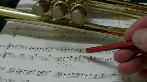 A-composer-making-notes-on-a-piece-of-sheet-music-with-a-pencil-with-a-brass-trumpet-in-the-background