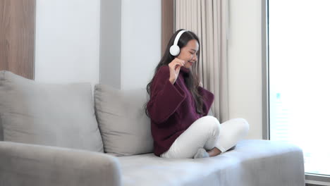 Sitting-on-a-couch-in-a-hotel-suite,-a-pretty-young-woman-wearing-headphones-dances-in-place