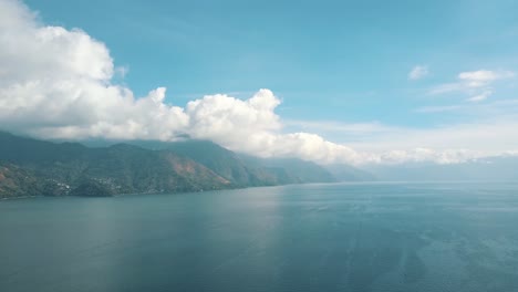 Drone-aerial-perspective-of-blue-lake-atitlan-during-sunny-day-with-clouds-in-the-mountains-in-Guatemala