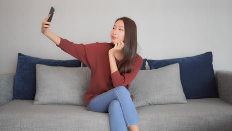 Eine-Junge,-Sehr-Attraktive-Frau-Sitzt-Auf-Einer-Couch-Und-Macht-Selfies-Aus-Verschiedenen-Blickwinkeln