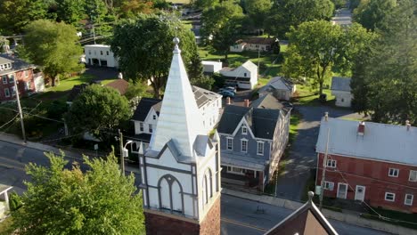 Aerial-tilt-reveals-church-steeple-along-road-in-old-historic-houses-in-USA,-Small-town-America,-August-summer-magic-hour-overhead-view