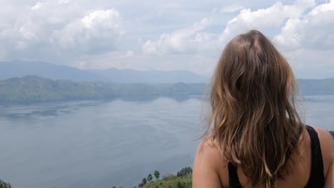 Ultra-slow-motion-shot-of-young-caucasian-woman-looking-at-Lake-Toba-from-Samosir-Island-in-North-Sumatra,-Indonesia