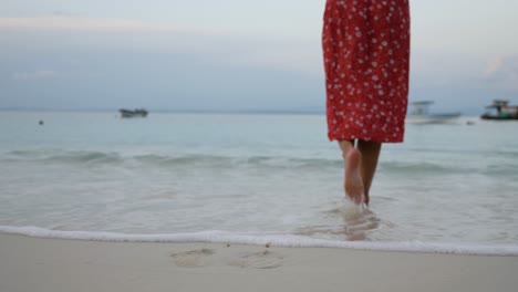 Slow-motion-shot-of-legs-and-bare-feet-of-caucasian-woman-in-red-dress-walking-into-the-sea-on-beach-at-Asu-Island,-North-Sumatra,-Indonesia