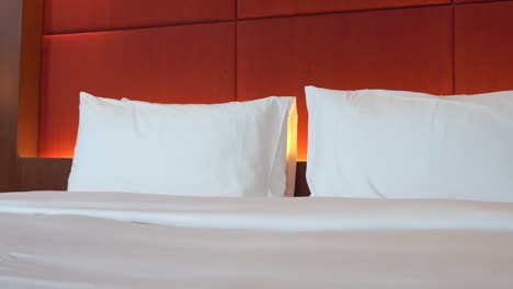 Modern-Bedroom,-Led-Light-Behind-White-Pillows-and-Kingsize-Bed-in-Upscale-Hotel-Pan-Left
