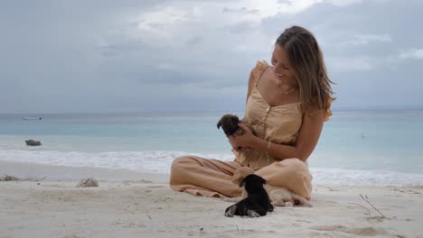 Ultra-slow-motion-shot-of-happy-caucasian-woman-playing-with-puppies-on-tropical-beach-at-Asu-Island,-North-Sumatra,-Indonesia