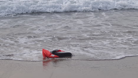 Empty-life-jacket-washes-ashore-beach,-slow-motion