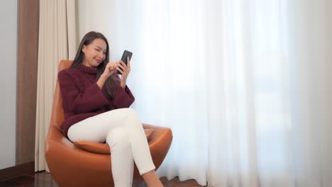 Sitting-in-a-modern-leather-chair-in-an-exclusive-hotel-suite-a-pretty-young-woman-texts-on-her-smartphone