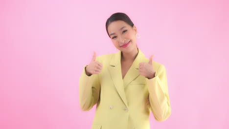 Medium-close-of-a-young-businesswoman-in-a-business-appropriate-suit-raises-her-hands-into-view-giving-the-thumbs-up-to-the-viewer