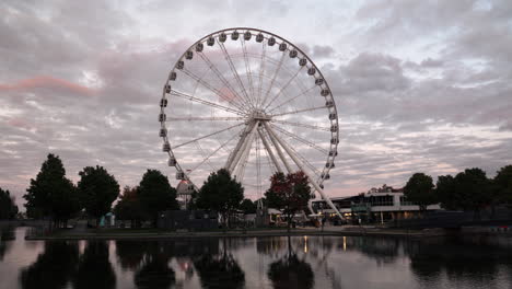 Grande-roue-de-Montreal---Ferris-Wheel-Spinning-With-Reflection-On-The-Water-During-Sunset-At-The-Old-Port-Of-Montreal-In-Quebec,-Canada---Coronavirus-Pandemic-Outbreak
