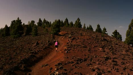 Aerial-shot-of-a-woman-going-up-a-trail-in-a-volcanic-landscape-in-a-sunny-day