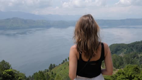 Ultra-slow-motion-shot-of-young-caucasian-woman-enjoying-view-of-Lake-Toba-from-Samosir-Island-in-North-Sumatra,-Indonesia